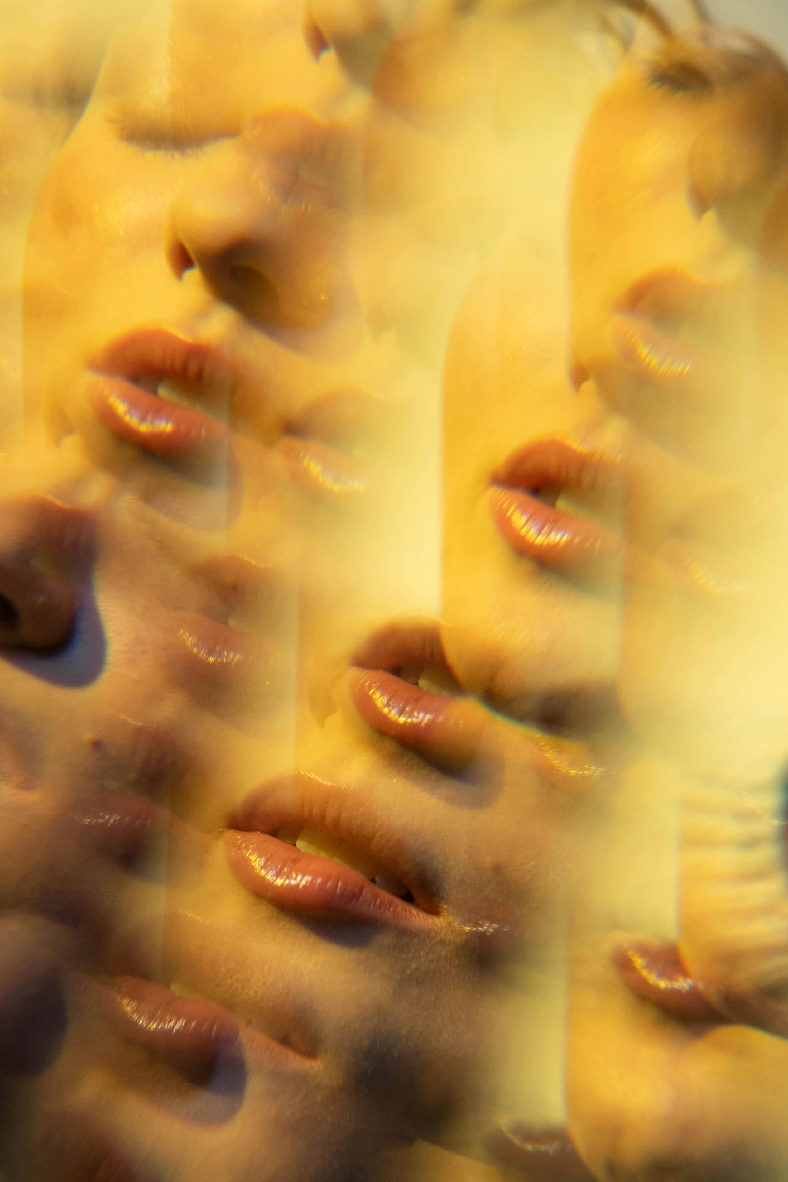 Multiple overlapping close-ups of a woman’s face and lips in warm yellow tones with a kaleidoscopic effect
